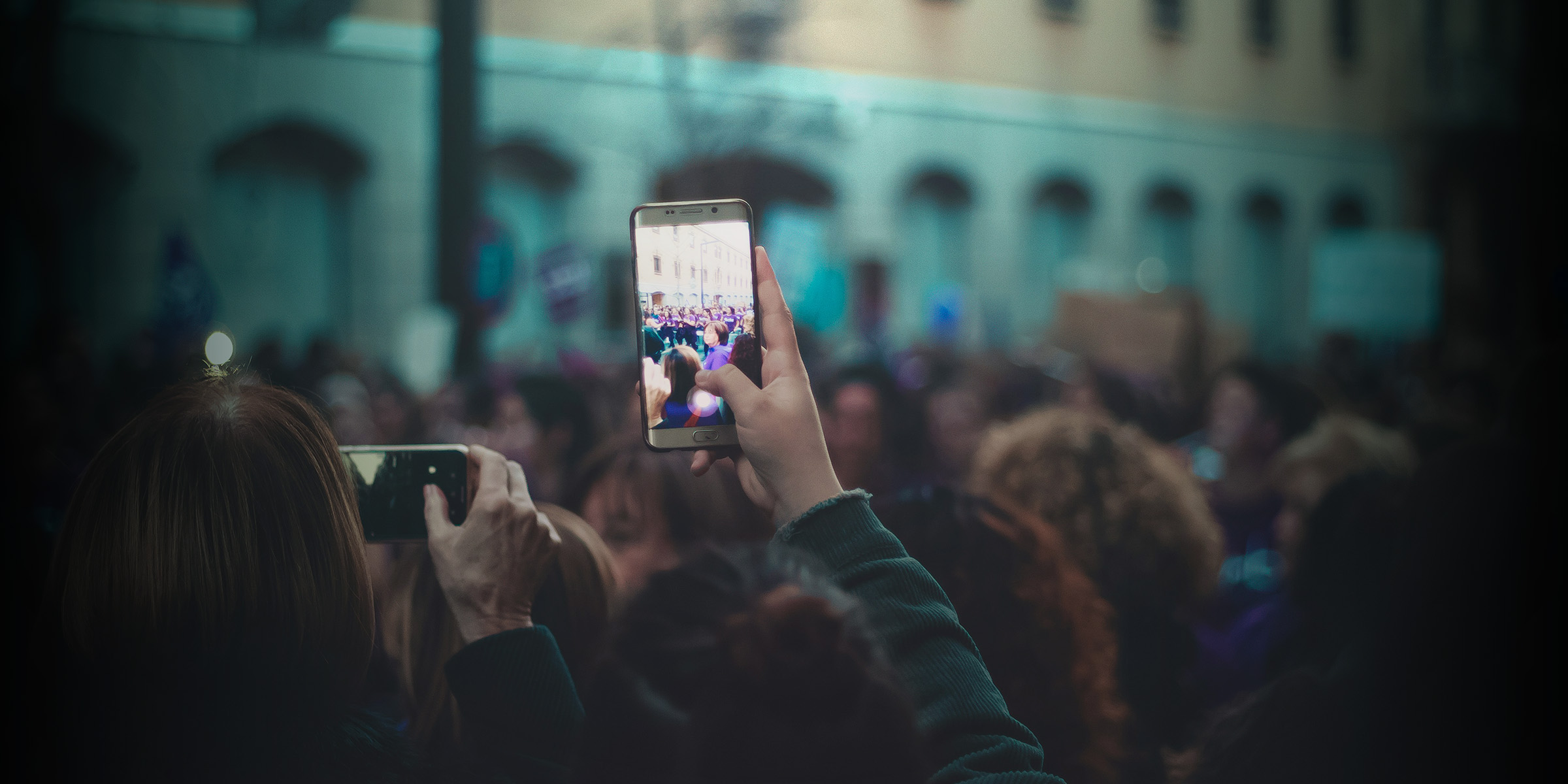 A hand lifts a phone above a crowd to record.